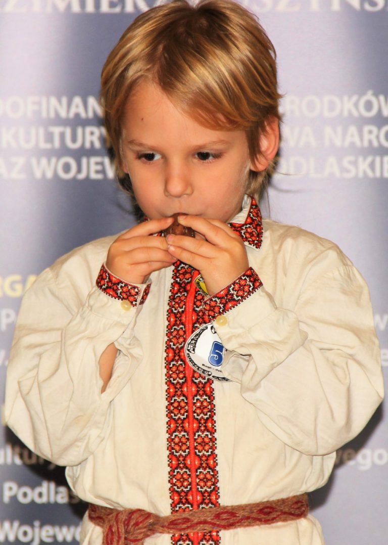 Młody chłopiec w stroju ludowym gra na okarynie.