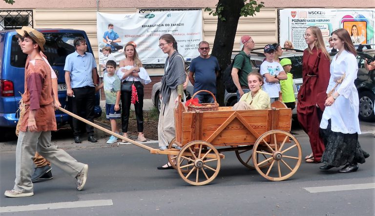 na zdjęciu osoby ubrane w stroje robocze ciągnące drewniany wózek