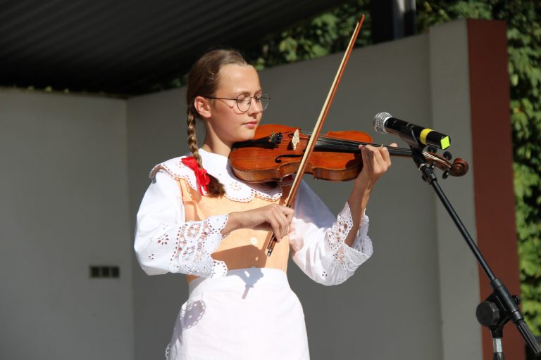 na zdjęciu dziewczyna w stroju ludowym grająca na skrzypcach podwiązanych