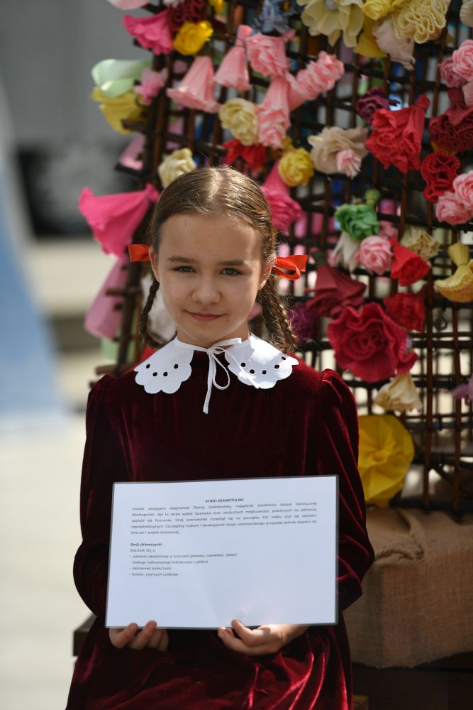 na zdjęciu dziewczynka w stroju ludowym trzymająca w rękach kartkę
