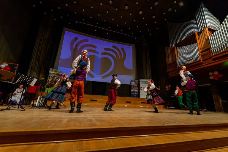 Na zdjęciu grpa młodzieży w strojach opoczyńskich. Tańczą na scenie.