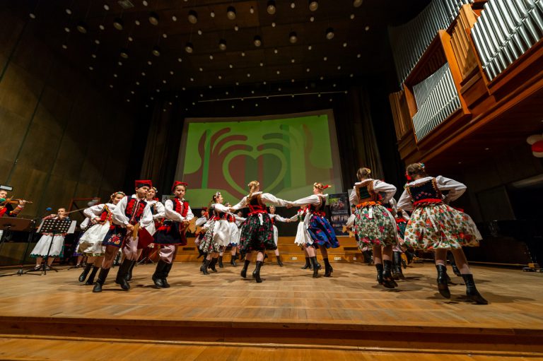Na zdjęciu grupa dzieci w strach krakowskich. Tańczą na scenie.