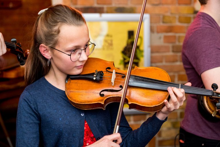 Na zdjęciu młoda dziewczyna gra na skrzypcach.