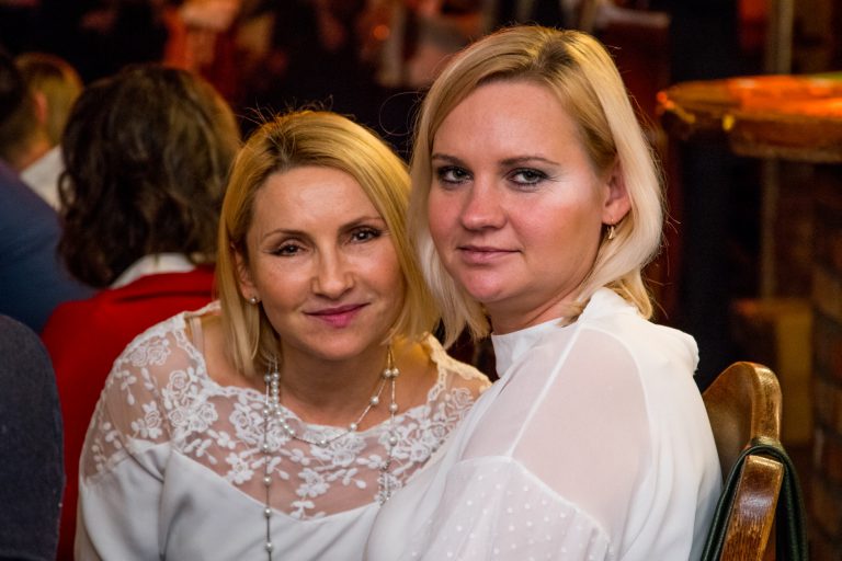 Dwie kobiety ubrane na biało uśmiechają się do obiektywu.