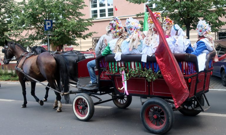 na zdjęciu wóz ciągniony przez konie a na nim osoby ubrane z stroje regionalne