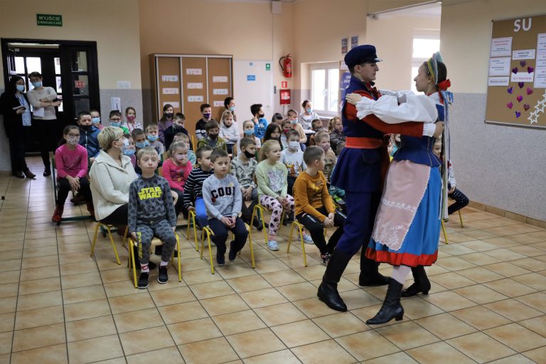na zdjęciu tancerze ubrani w stroje regionalne prezentują się przed dziećmi