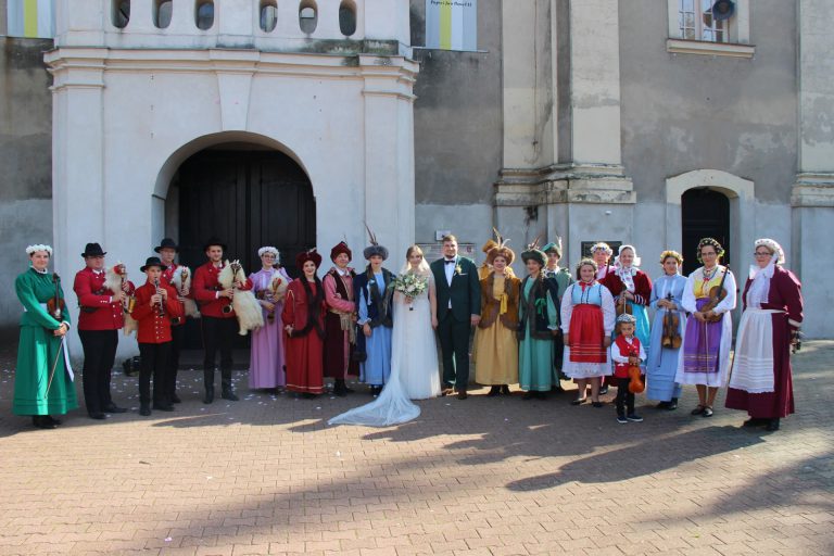 na zdjęciu para młoda i zaproszeni goście ubrani w stroje regionalne przed kościołem