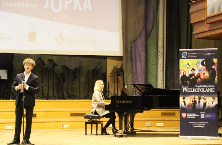 Na zdjęciu młody mężczyzna śpiewa do mikrofonu. Obok niego kobieta gra na fortepianie.