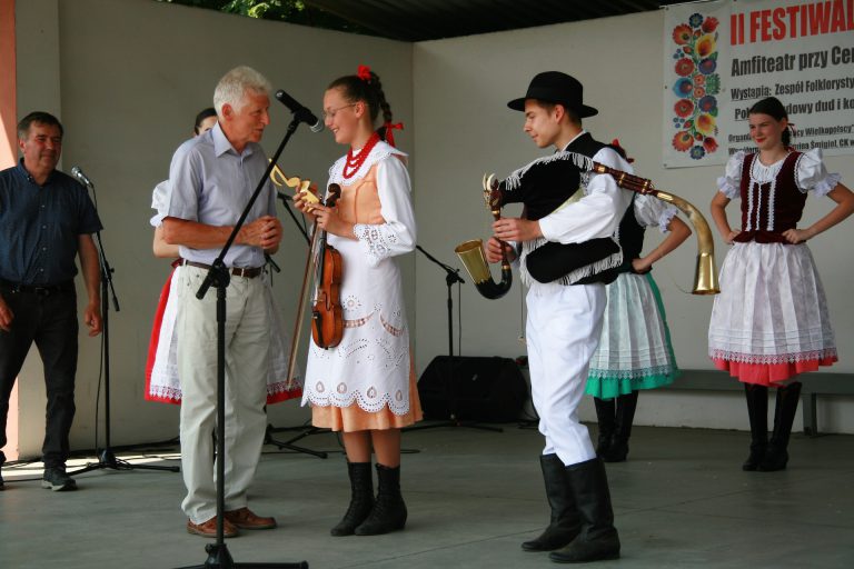 na zdjęciu mężczyzna wręczający nagrodę młodym muzykom grającym na tradycyjnych wielkopolskiech instrumentach