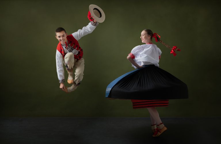na zdjęciu chłopak skaczący przez nogę i kręcąca się dziewczyna ubrani w stroje regionalne