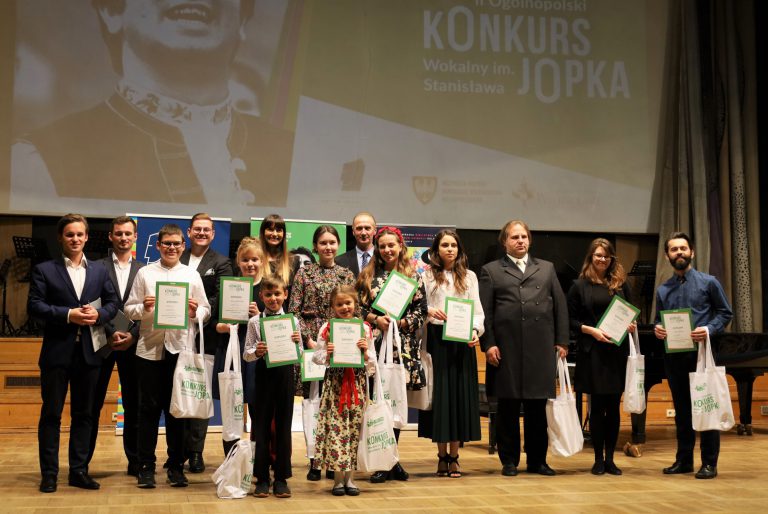 na zdjęciu grupa osób stojąca na scenie z dyplomami i nagrodami w rękach